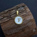 Close-up of golden letter F pendant with white shell inlay on natural wood background - Letter F / 17x20mm