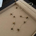 Close-up of tiger eye stone cross pendant necklace with golden metal beads and fine chain - Long Tiger Eye Gold Faceted Bead Necklace