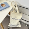 Detail van gebroken witte canvas shopper met blauwe letteropdruk op een acryl stoel - Broken Wit