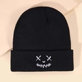 Close-up of black knitted beanie featuring white embroidered funny face design with X eyes - Smile Face Embroidery - Black
