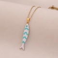 Macro de un collar dorado con colgante de pez esmaltado blanco y turquesa en tela beige - Pez de Rayas Blancas