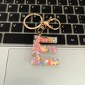 Letter E resin keychain with colorful heart sequins and gold ring on a laptop - Letter E