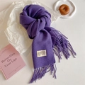 Detailed macro view of soft purple fringe scarf with woven brand tag on white surface - Purple