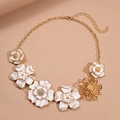 Elegante collar dorado con flores de esmalte blanco y cristales sobre fondo rosa suave - Dorado con Circonita