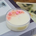 Handmade scented candle with pink dried flowers in a clear jar on a decorative book - Peach Blossom