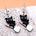 Close-up of resin black cat on broom earrings resting on a rustic stone texture - Cat on Broom