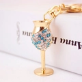Elegant gold wine glass keychain with sparkling blue and white rhinestones on white books - Blue
