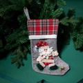 Calza di Natale grigia con babbo natale e risvolto scozzese rosso appesa a un ramo - Babbo Natale