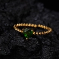 Macro detail of a heart-shaped green gemstone ring on a dark textured rock background - Natural Diopside Gold