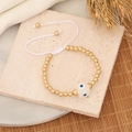 Detail of beaded evil eye bracelet with golden beads and white adjustable cord on stone base - White