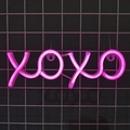 Neon LED XOXO sign with pink glowing lights mounted on a black mesh wall grid - Pink