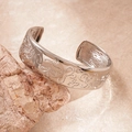 Detail of silver-toned relief engraving on an oval open cuff bracelet over a stone - Silver