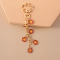 Detail showing red and yellow daisy charms on a golden metal keychain link - Red Flower