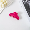 Detail view of a glossy fuchsia acetate hair claw clip on a minimalist white background. - Red