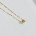 Dettaglio di una collana d'oro con pendente cilindrico in zircone su sfondo in pelle bianca - Bianco