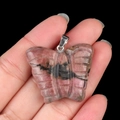 Ciondolo a farfalla in rodonite naturale con venature rosa e nere nella mano - Rodonite
