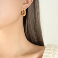 Elegantes pendientes de aro en forma de C dorados y retorcidos usados por una modelo - Dorado