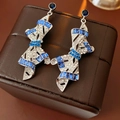 Detalle de pendientes de lazo plateado con cristales azules sobre un joyero elegante - Plata-Azul (Pin de Plata S925)