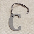 Detailed view of grey pebble leather letter C bag charm on a beige linen background - C Letter Gray