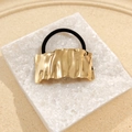 Golden irregular wave metal hair tie with black elastic rope on white stone display - Rectangular Pleated Hair Tie