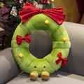 Green plush Christmas wreath pillow with red bow and cute smiling face on a sofa - New Wreath