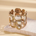 Detail eines unregelmäßigen goldenen Armreifs mit Marmor-Emaille auf einer Steinoberfläche - Gold