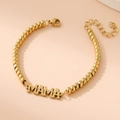 Detalle macro de pulsera de cuentas bañada en oro 18K con colgante MAMA pulido - Letra MAMA / Dorado