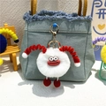 Detail of cute white plush monster keychain with red horns on a blue denim bag - White