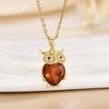 Macro detail of golden owl necklace featuring a heart-shaped orange crystal and shiny gems - Gold Owl/Heart Orange Brown Gem