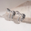 Dettaglio macro di orecchini a fiocco d'argento con texture metallica liscia e design 3D - Argento