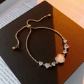 Détail du bracelet coeur en or avec pierres zircons sur fond sombre avec des livres - Doré