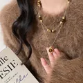 Collana doppia dorata con pendente in occhio di tigre e perle su maglione marrone - Collana a Doppio Strato con Perline e Ciondolo Rotondo in Occhio di Tigre