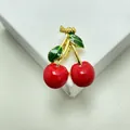 Vista macro di una spilla a ciliegia con foglie verdi e un elegante fiocco dorato - Stile 9 (Rosso/Verde/Oro)