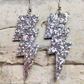 Dettaglio di orecchini a forma di fulmine glitter argento su una superficie di pietra - Paillettes Argento