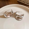 Gros plan de boucles d'oreilles argentées en forme de C sur une assiette en céramique - Argenté