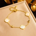 Elegante pulsera de acero dorado con colgantes de nácar blanco sobre un cojín con textura fina - Pulsera (B1437)