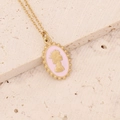 Dettaglio ravvicinato di una collana con medaglione dorato e cammeo rosa su sfondo in pietra - Rosa