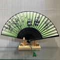 Green folding fan with panda and bamboo pattern, black hollow frame, and matching green tassel - Charming Naivety