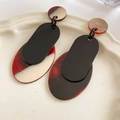 Dettaglio di orecchini pendenti geometrici in resina tartarugata su un vassoio di ceramica - Ago in Argento-Nero-Caffè