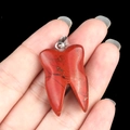 Hand holding a natural red agate stone tooth pendant with silver bail on black background - Red Jasper