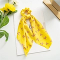 Macro detail of yellow satin scrunchie with leaf print and streamers on white desk - Yellow Leaves