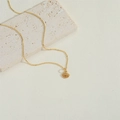 Collana dorata con ciondolo malocchio e zirconi colorati su un blocco di pietra beige - Arancione