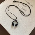 Minimalist black headphone pendant necklace displayed on an artistic vintage book cover - Black