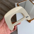 Dettaglio del fermaglio per capelli in acetato beige con forma a D e stampa nera Do - Bianco Crema D Molletta