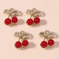 Dettaglio di quattro ciondeli a ciliegia rossa in lega con foglie dorate e strass lucidi - Combinazione fiocco