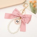 Pink ribbon bow keychain with white pearl wrist strap and gold floral pendant charm - Pink