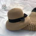 Sombrero de paja beige oscuro con elegante lazo negro sobre fondo de seda blanca - Caqui