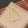Dettaglio di orecchini a triangolo dorati con gemme su sfondo di libro d'epoca - Stile Triangolo