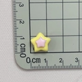 Makroaufnahme von 1cm zweifarbigem Stern-Harz-Accessoire mit Maßskala auf Gittermatte - Gelb