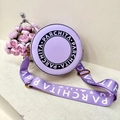 Chic lavender round crossbody bag with logo strap and circular emblem on stone background - Purple
